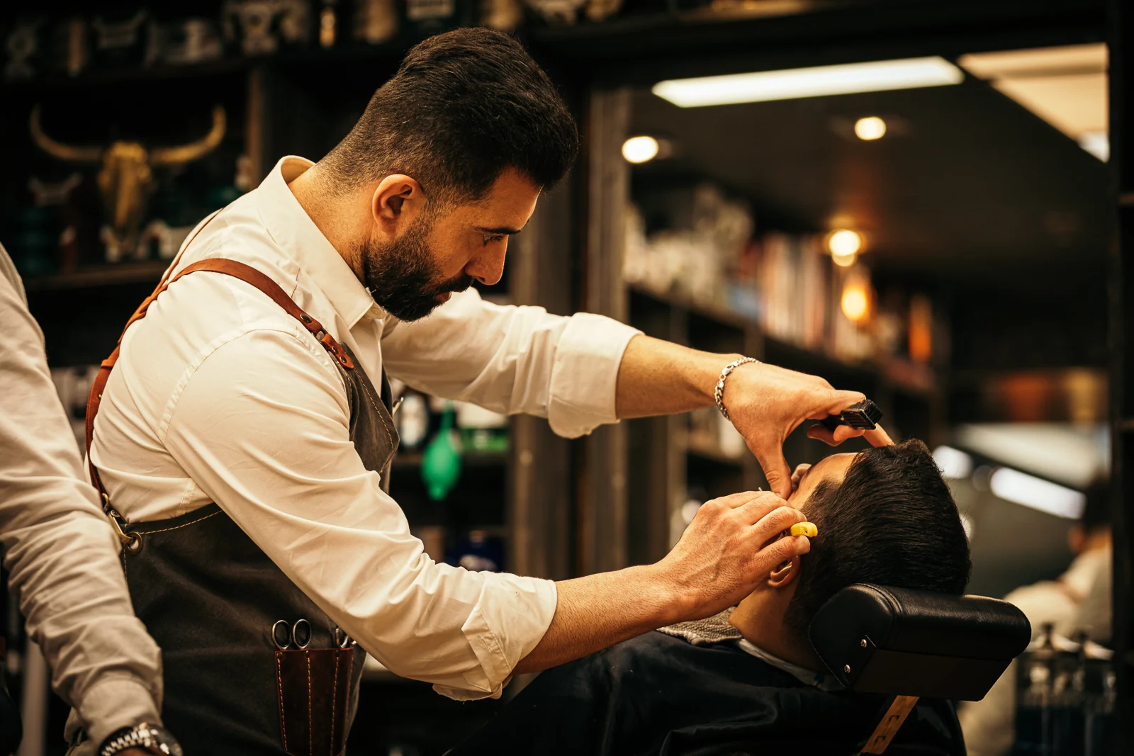 Barberare arbetar med rakkniv i den varmt upplysta salongen
